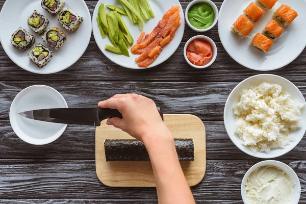 a hand holding a sushi knife preparing to cut the roll of sushi on the board